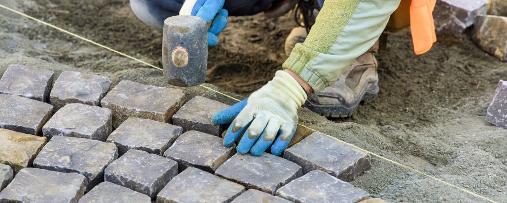 manos de obrero colocando piedras de baldosines en una calle