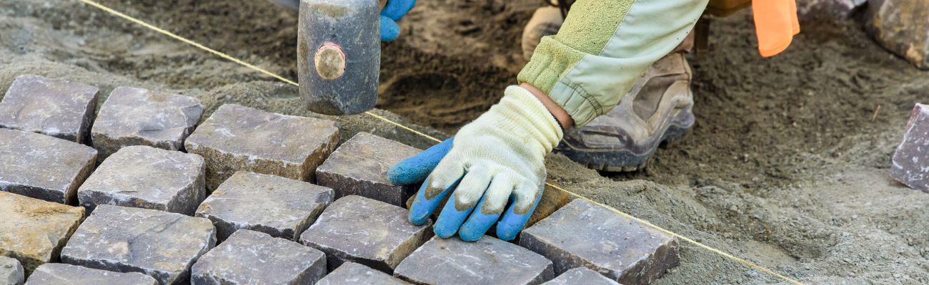manos de obrero colocando piedras de baldosines en una calle